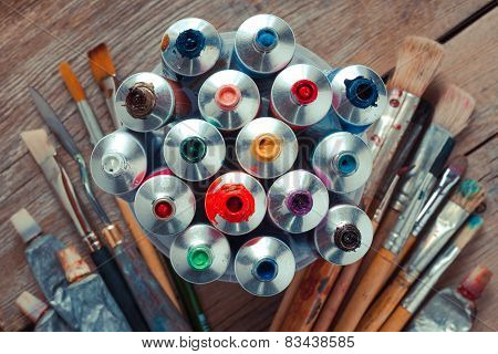 Vintage Stylized Photo Of Oil Multicolor Paint Tubes Closeup And Artist Paintbrushes On Wooden Desk.