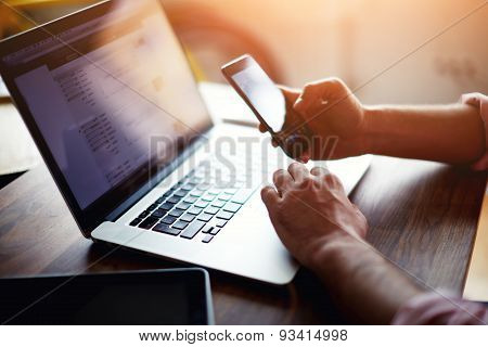 Side view of a man's hands using smart phone in interior  at his coworking place using technology