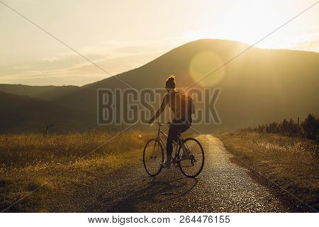 Cycling In Sunset. Lifestyle Concept. Hipster Woman Cycling In Sunset In Countryside. Healthy Lifest