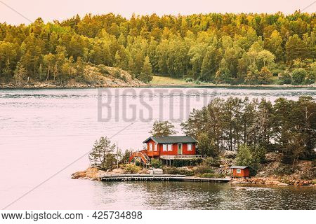 Sweden. Many Beautiful Red Swedish Wooden Log Cabin House On Rocky Island Coast In Summer. Lake Or R