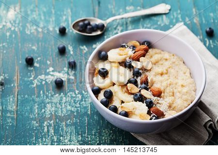 Bowl of oatmeal porridge with banana, blueberries, almonds, coconut and caramel sauce on teal vintage table. Hot and healthy food for Breakfast.