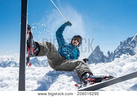 Cheerful man playing with snow while sit with ski. Happy smiling skier enjoying sitting on snow with ski equipment. Man having fun on snowy mountain.