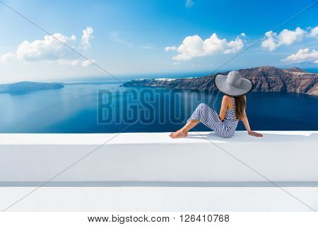 Europe Greece Santorini travel vacation. Woman looking at view on famous travel destination. Elegant young lady living fancy jetset lifestyle wearing dress on holidays. Amazing view of sea and Caldera