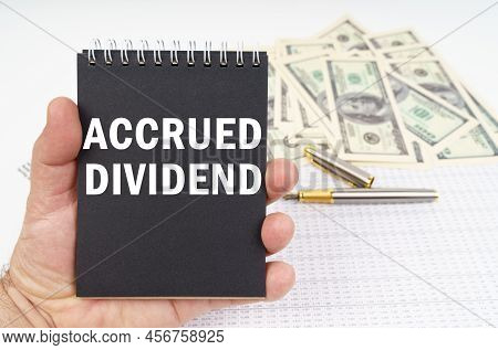 Business Concept. In The Man's Hand Is A Notepad With The Inscription - Accrued Dividend, In The Bac