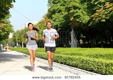 Running couple runners jogging in city park. Exercising woman and man runner training together on run living healthy active lifestyle in Buen Retiro Park, Parque el Retiro in Madrid, Spain, Europe.