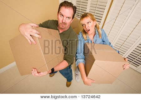 Obviously Exhausted Couple Holding Moving Boxes in Empty Room.