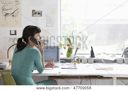 Young female artist using cell phone at desk