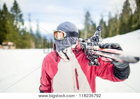 Young man holding ski at ski resort.Skier holding skis looking at the mountains.Side view of handsom