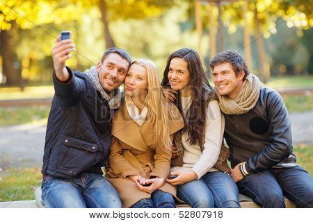 summer, holidays, vacation, travel and tourism concept - group of friends or couples having fun with smartphone photo camera in autumn park