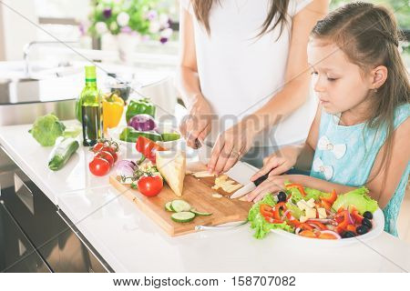 Cute little girl cooking with her mother. Healthy food, cooking healthy salad with vegetables ingredients. Mom and daughter cooking together. Recipe food for baby or child