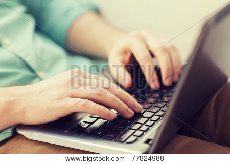 technology, home and lifestyle concept - close up of man working with laptop computer and sitting on sofa at home