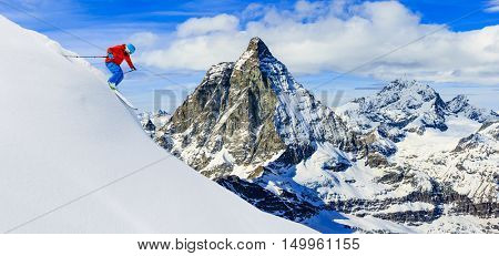 Skier skiing downhill in high mountains in fresh powder snow. Snow mountain range with Matterhorn in background. Zermatt Alps region Switzerland.