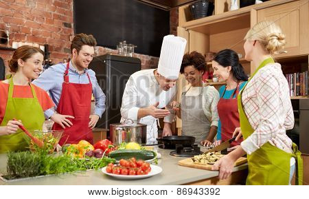 cooking class, culinary, food and people concept - happy group of friends and male chef cook cooking in kitchen