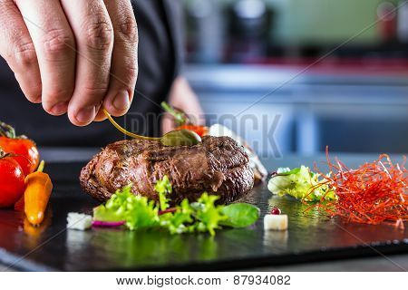 Chef in hotel or restaurant kitchen cooking, only hands. Prepared beef steak with vegetable decorati