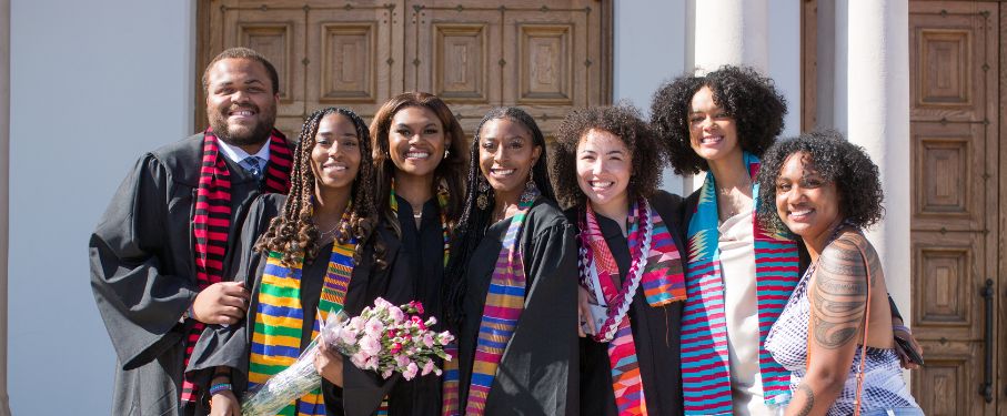 Graduates in regalia and African stoles pose outside of the chapel.